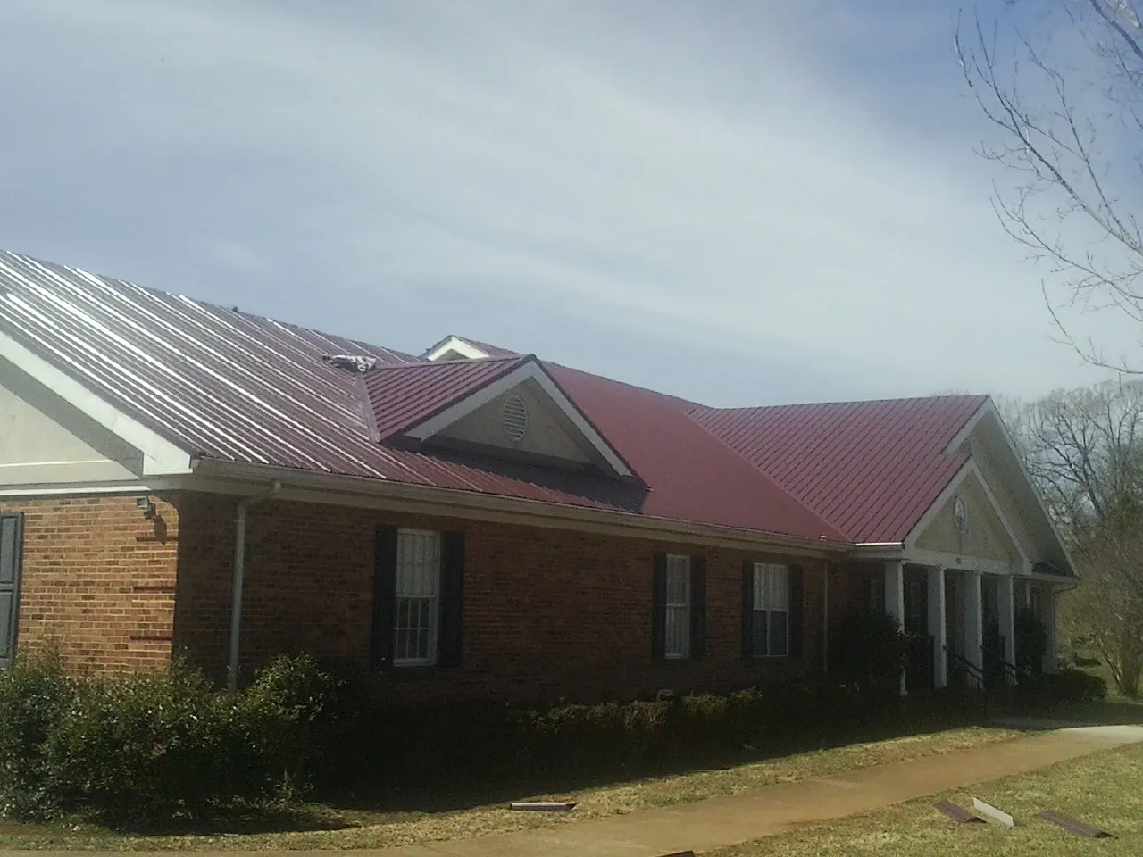 Red metal roof with gabled entries on a long brick building, from a Hail Damage Roof Repair job in Sarver