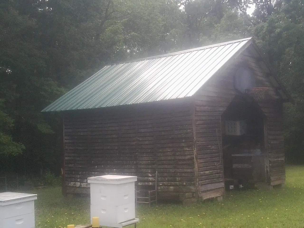Green metal roof on a weathered barn beside stacked beehives in Sarver