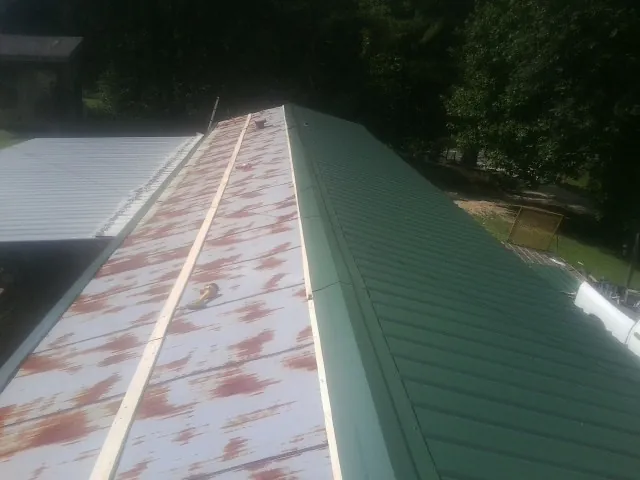 Old rusted panels beside newly installed green metal roofing — Wind Damage Roof Repair by Roofing Brothers in Sarver