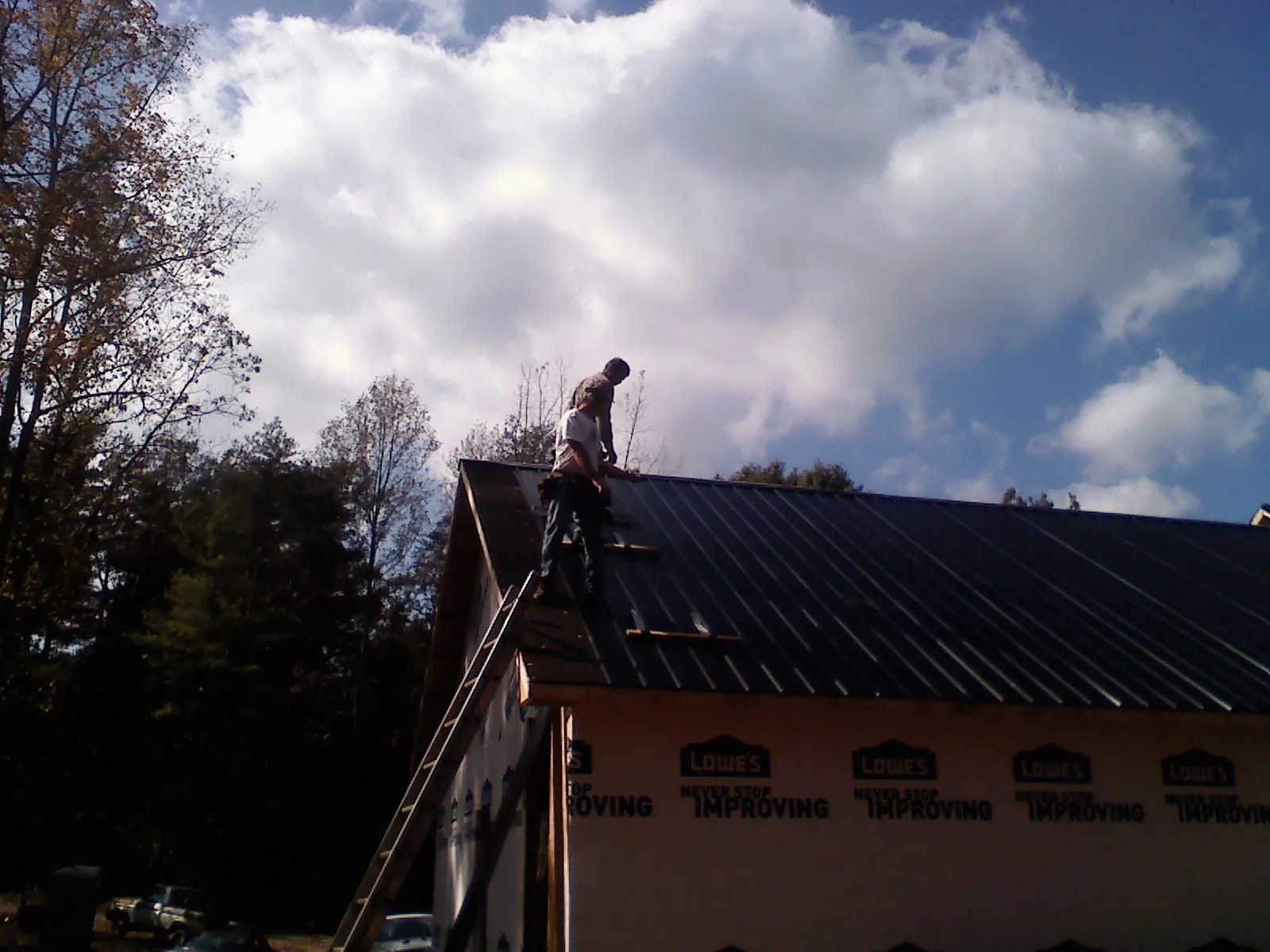 Roofer fastening dark metal panels high against a cloudy sky, from a Roof Inspection job in Sarver
