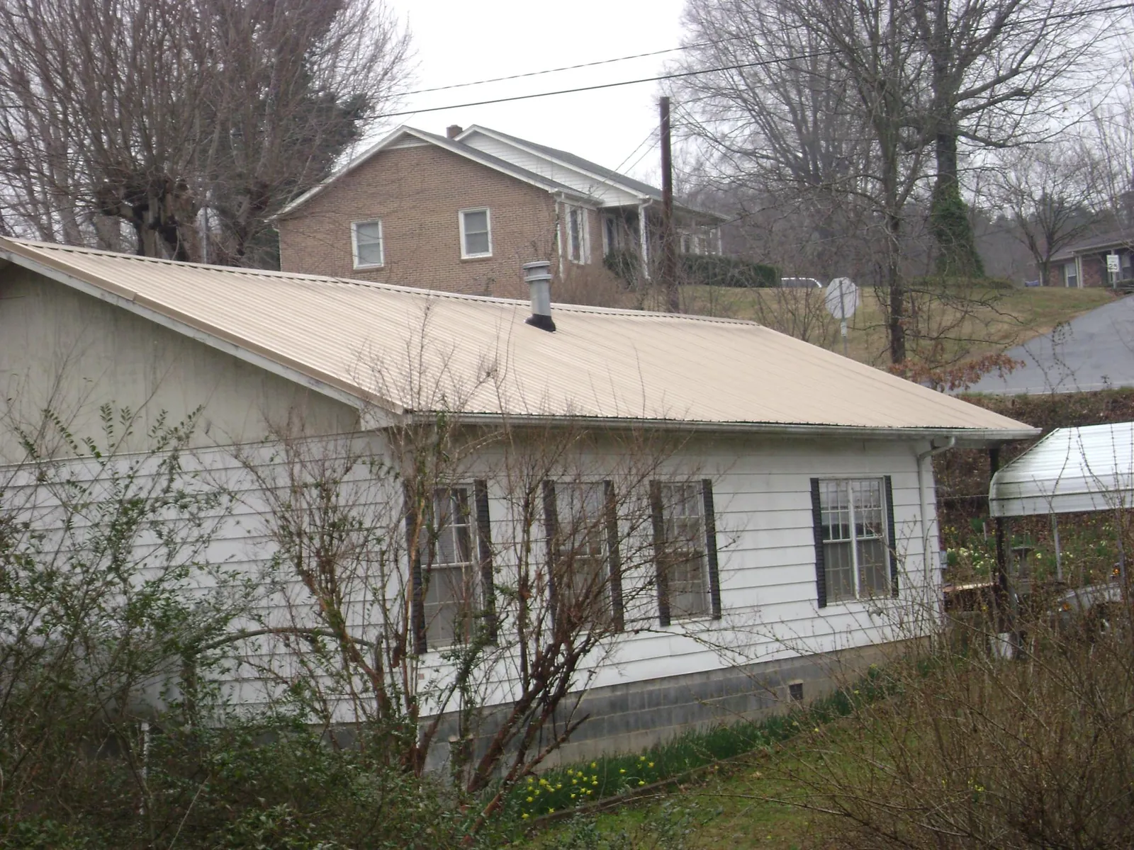 Tan metal roof on a white sided house set into a hillside — Commercial Roofing by Roofing Brothers in Sarver