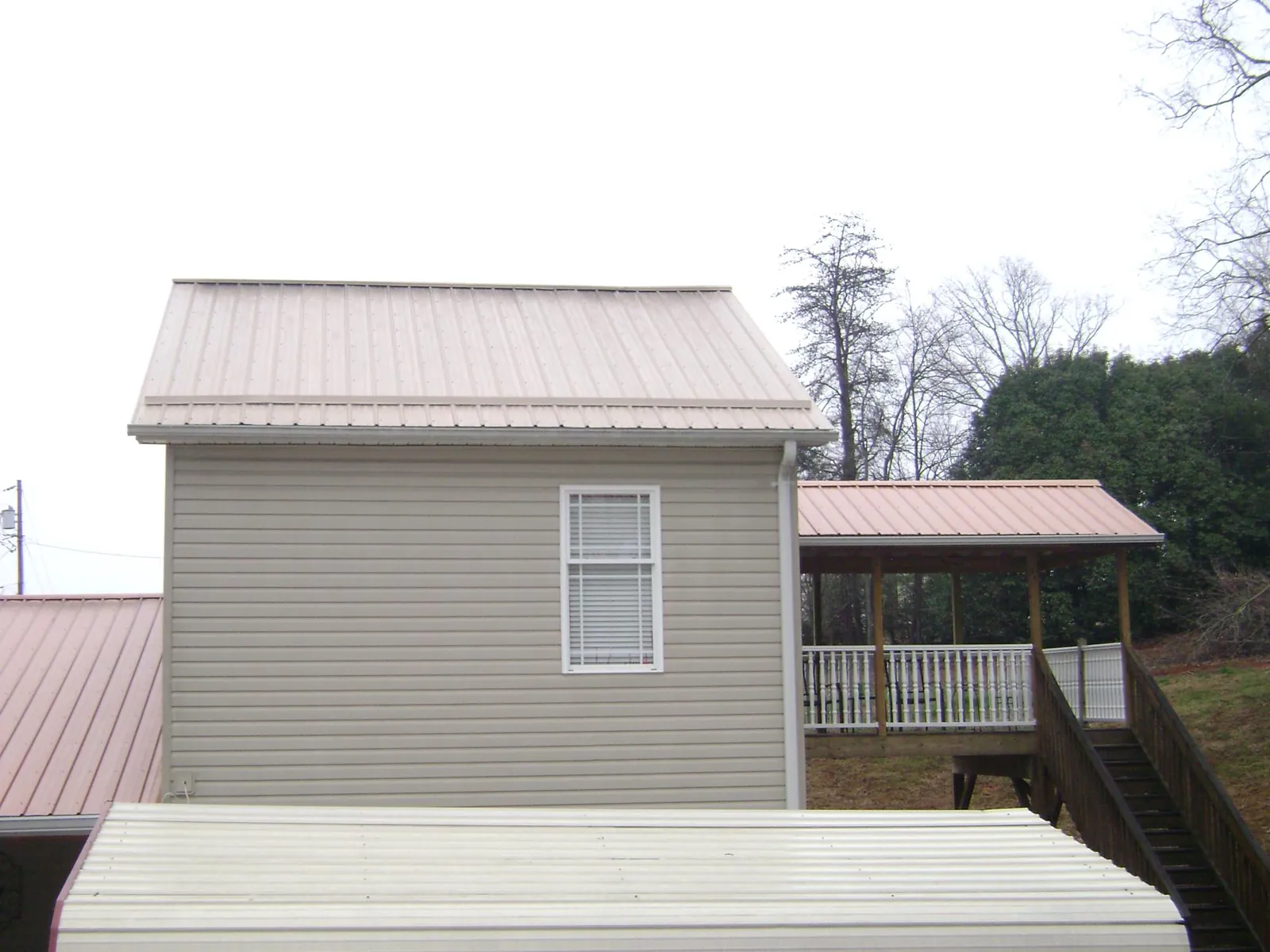 Tan metal roofs on a two story addition and attached porch, from a Roof Replacement job in Sarver